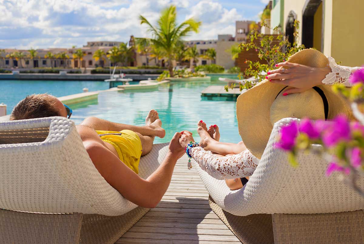 hotel guests sun bathing by luxury resort pool